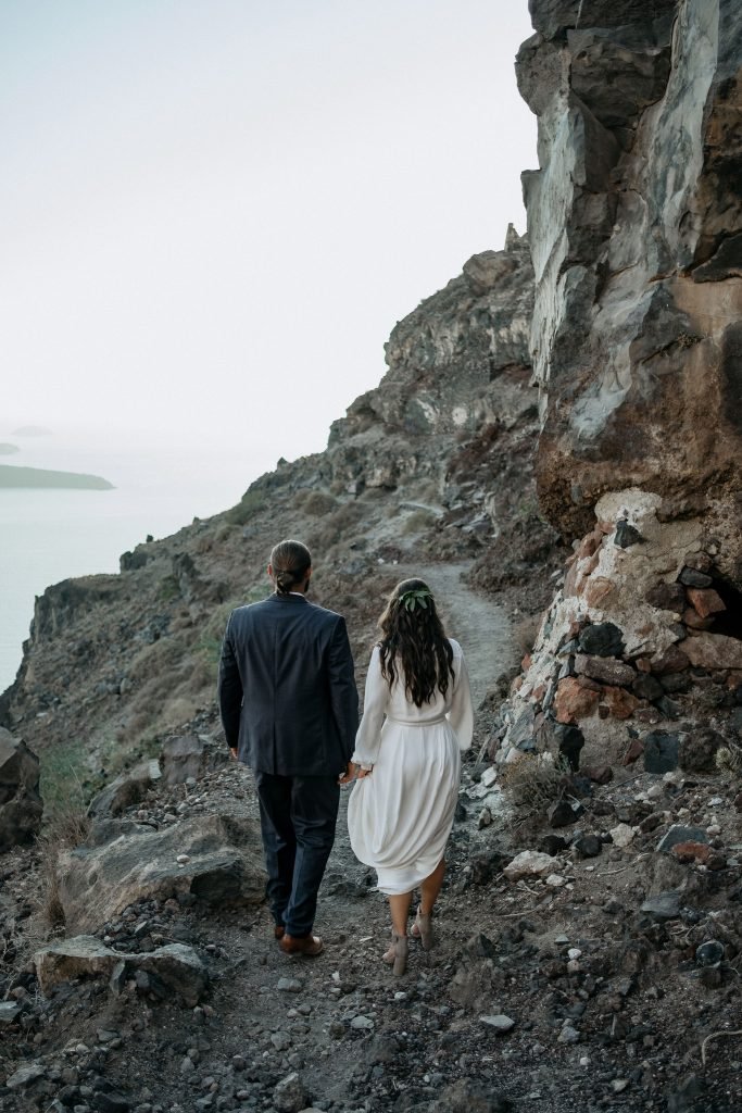 stylish Santorini elopement couple walking hand in hand on the mountain