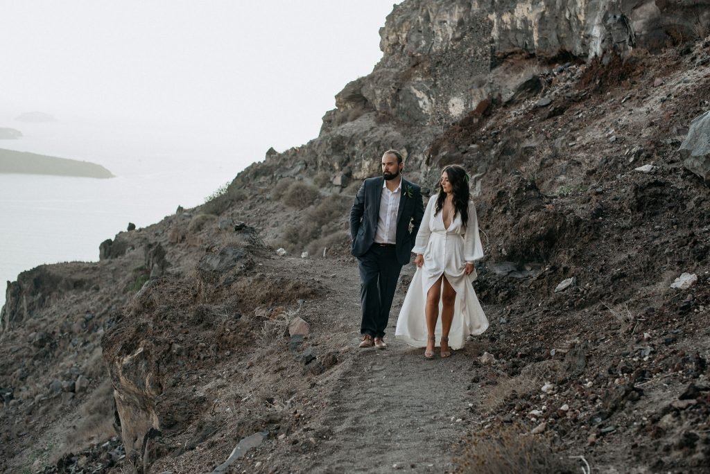 stylish Santorini elopement couple walking hand in hand on the santorini mountain