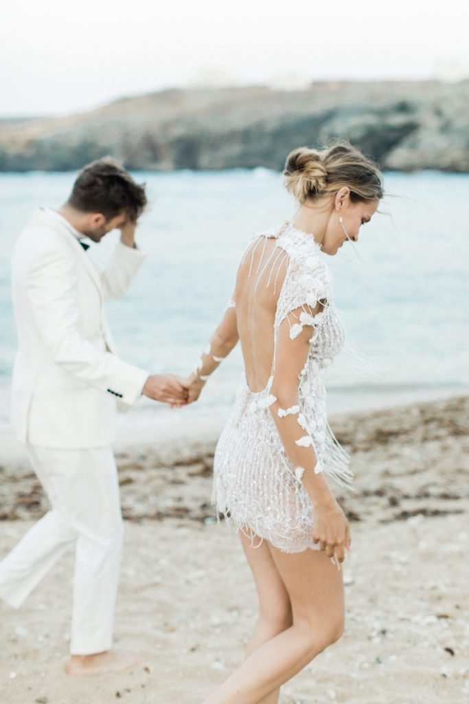 Bride in Mairi Maprola dress Love Story in Mykonos holding a grooms hand