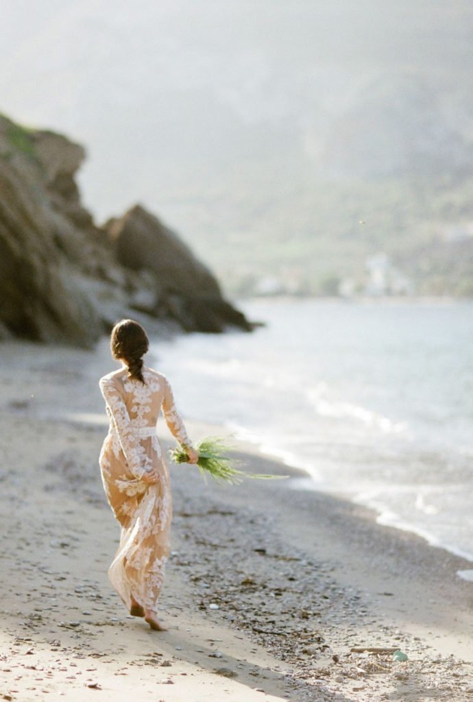 Boho Bride walking down the beach by the rocks