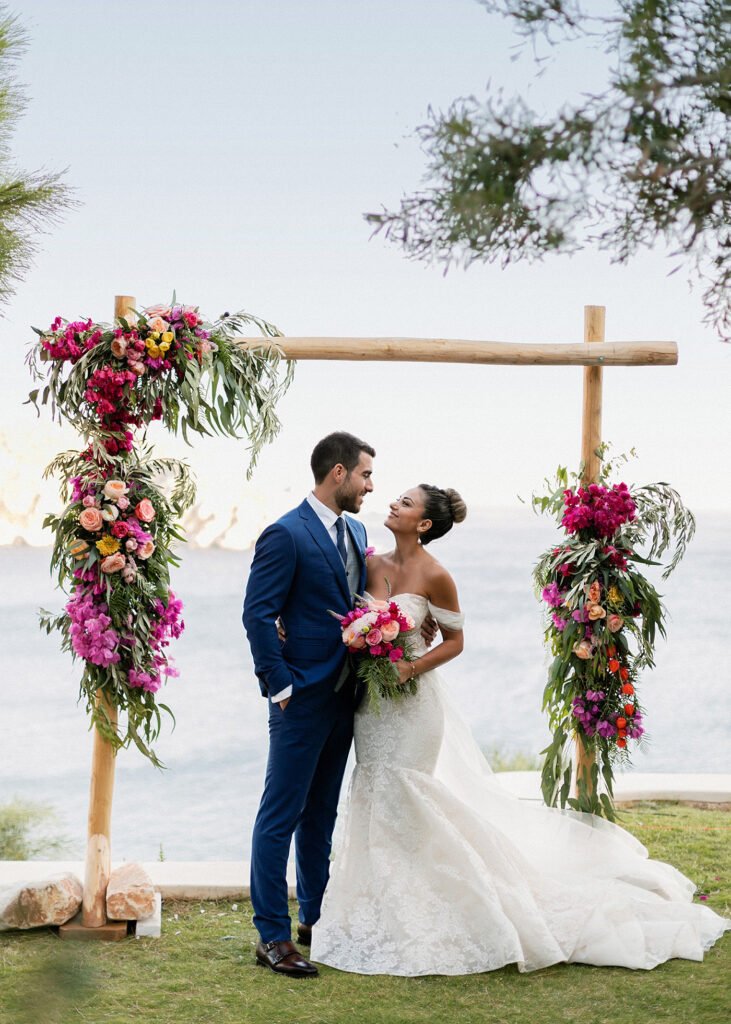 Afghan bride and Greek Groom standing under the ceremony arch for their Fun and colorful modern island wedding