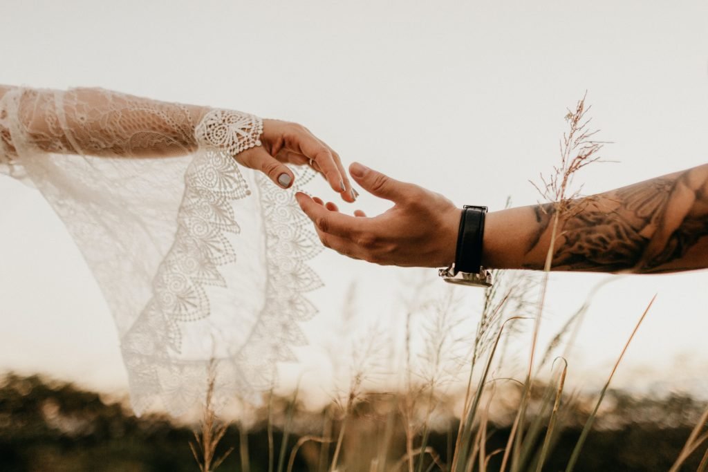 Woman's and Man's hand in the air  among tall grass, reaching out to each other to touch for their wedding 