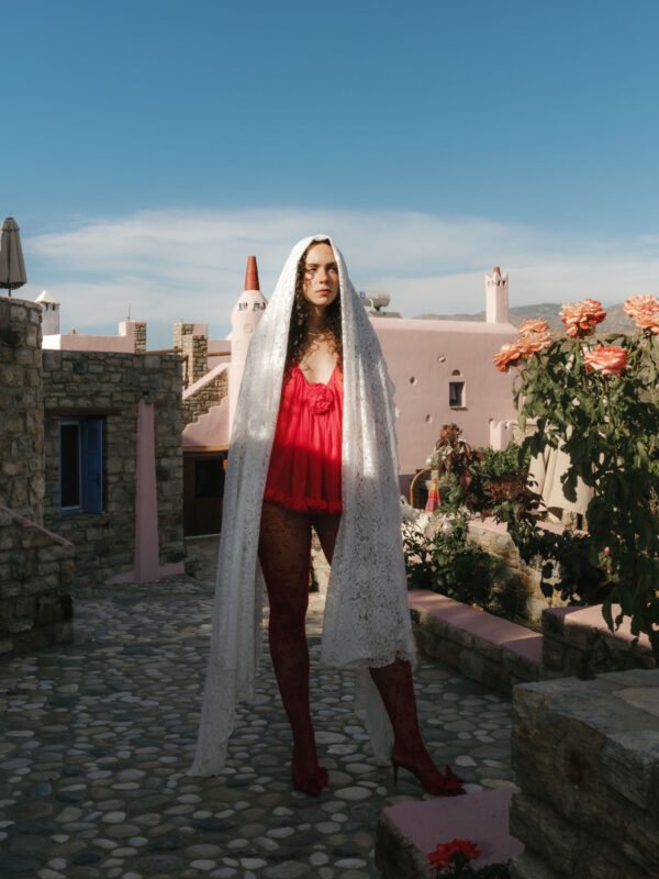 No-Décor No-Venue Wedding in Naxos Bride standing in front of a unique pink villa in Red Dress and white lace veil