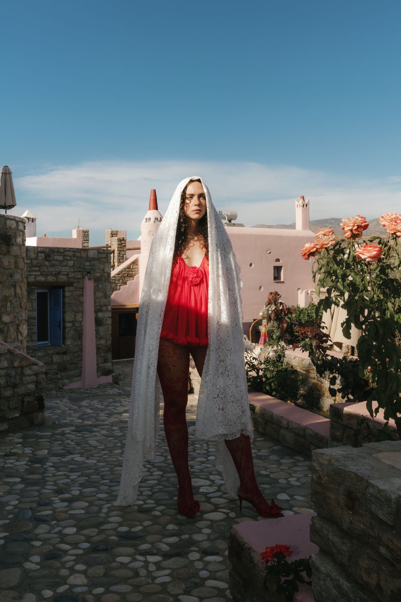 No-Décor No-Venue Wedding in Naxos Bride standing in front of a unique pink villa in Red Dress and white lace veil