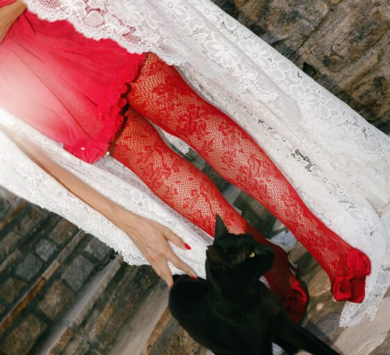 Bride dressed in red dress and white lace veil petting a black cat at her no-decor wedding in Naxos island in Greece