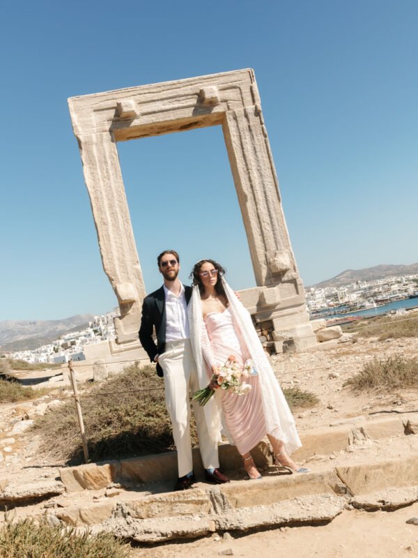 Things to consider for a wedding on a Greek island. Groom and bride standing in front of Naxos Portara monument