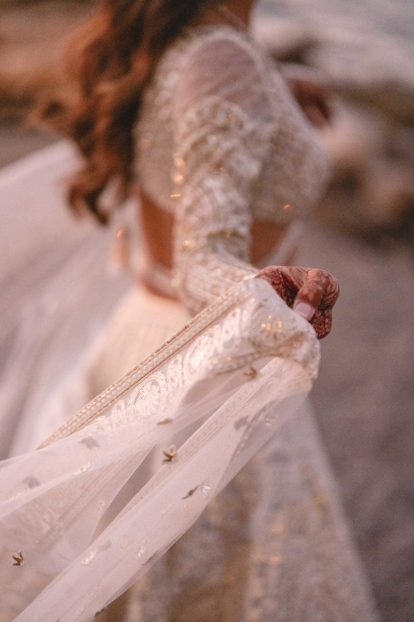 Closeup of bride wearing a white gold foil Falguni Shane Peacock Lehenga and her hand with henna tattoos 