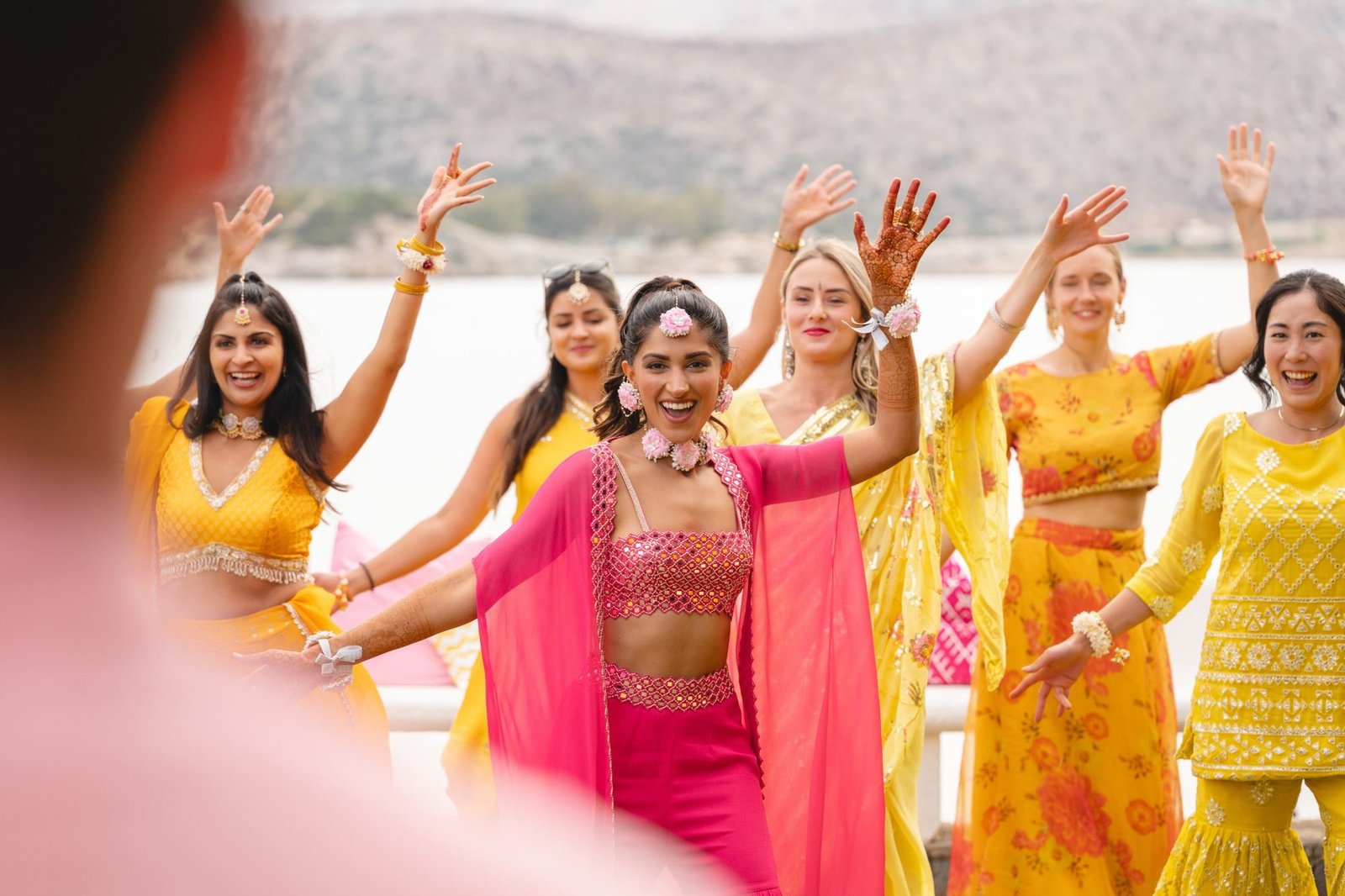 Bride in pink dress smiling and dancing with her guests in yellow during her beachfront Haldi and Mehndi celebration in the Athenian Riviera