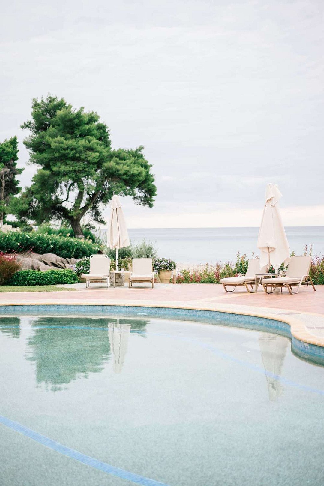 White and pastel wedding reception pool décor surrounded by Mediterranean greenery.