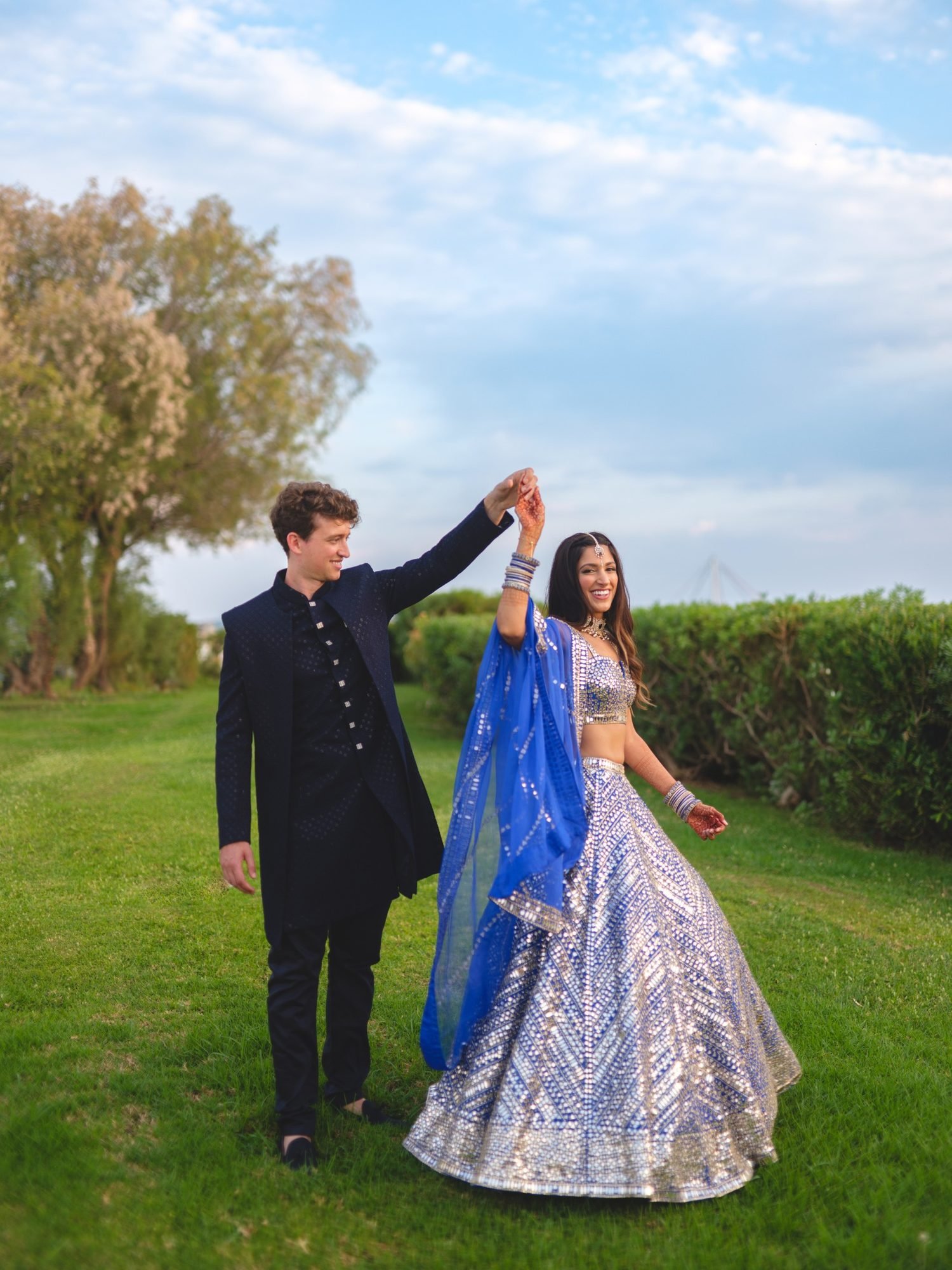 Bride wearing a royal blue mirror embroidery Seema Gujral Lehenga dancing with the groom in navy blue suit at an outdoor Sangeet venue