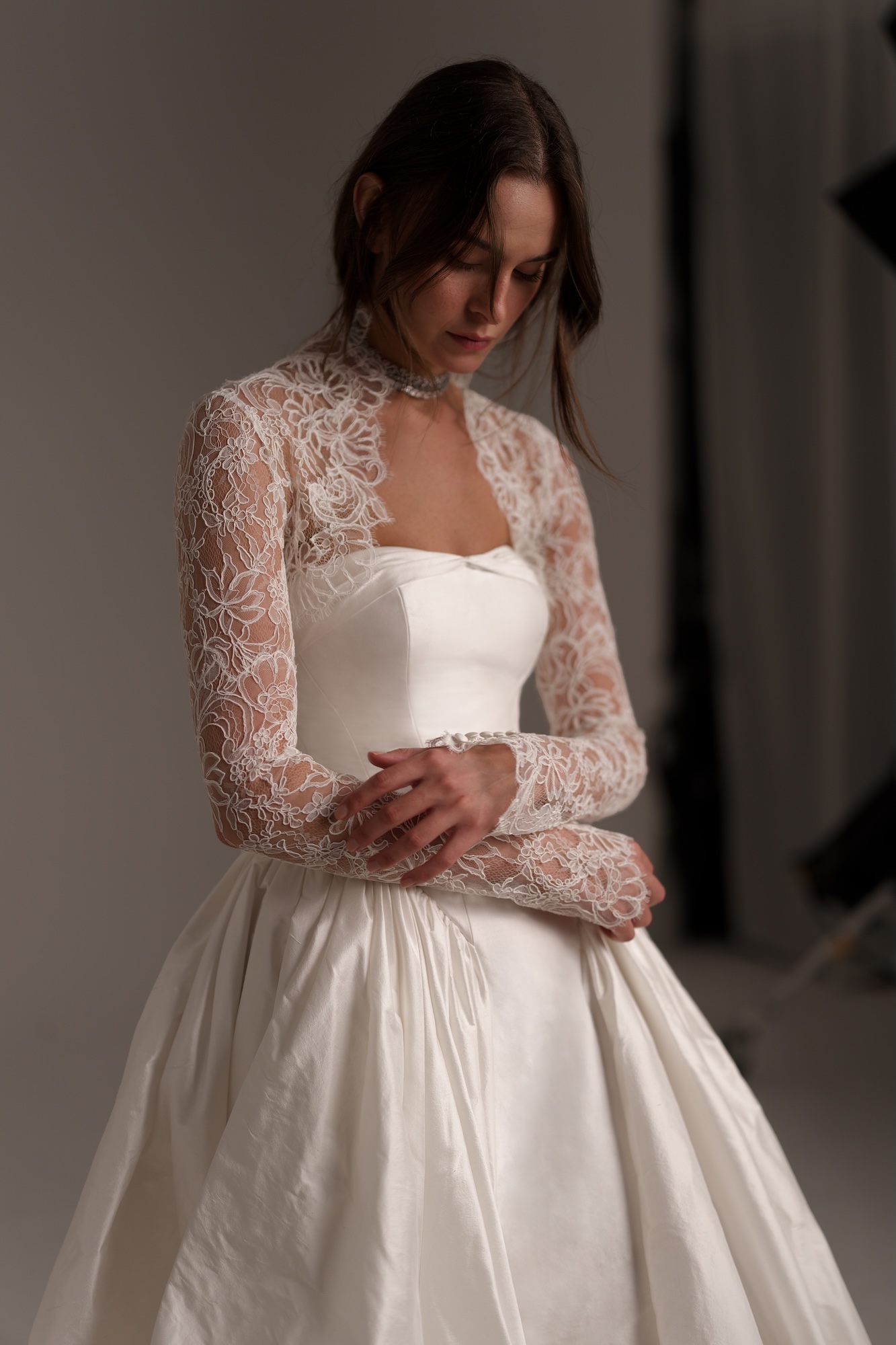 Nelly by Lihi Hod, strapless silk Shantung ball gown with architectural folds and a dropped waist topped with delicate floral lace long sleeves