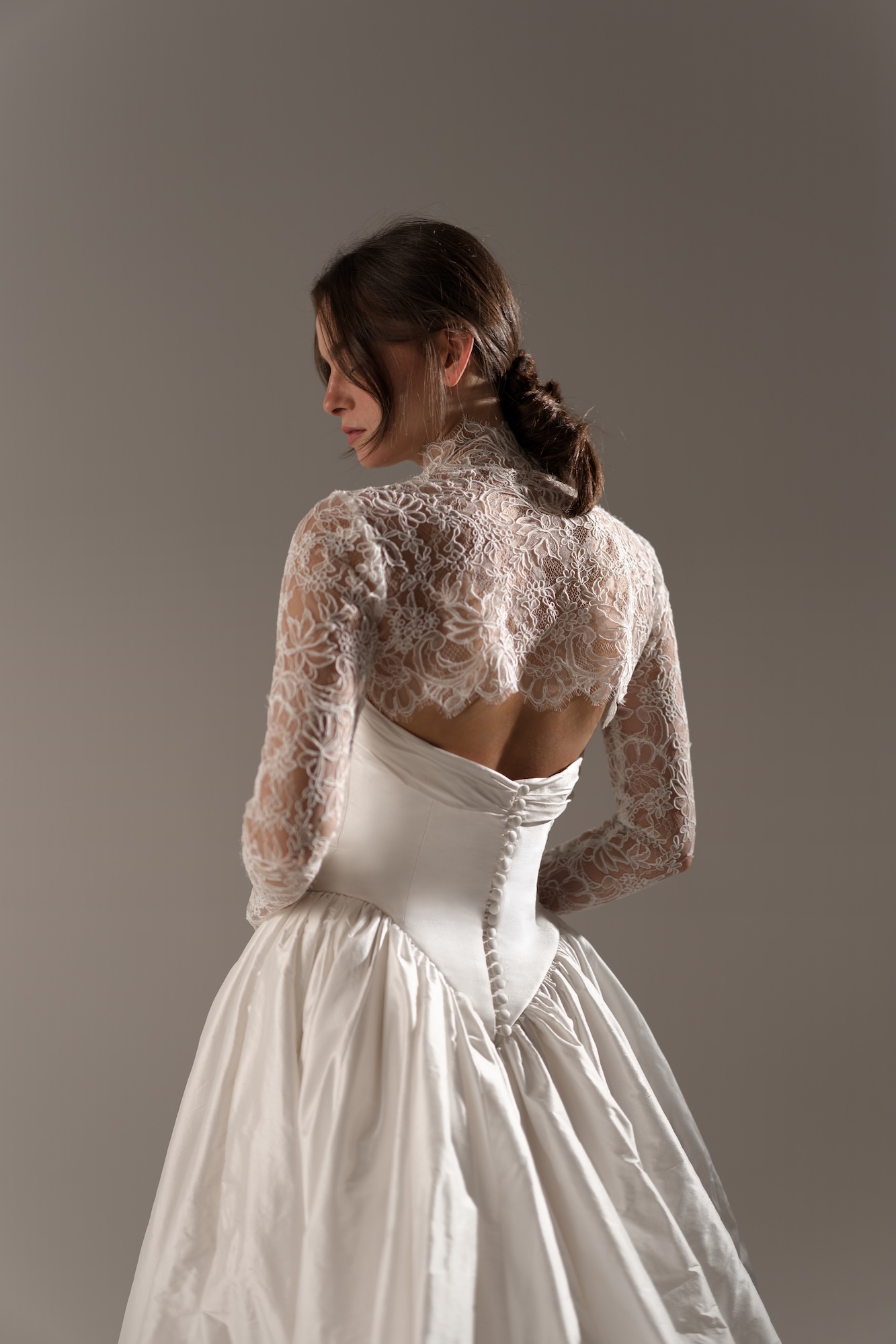 Back of Nelly, dreamy wedding dress by Lihi Hod featuring a dramatic silk Shantung ball gown, strapless sweetheart bodice topped with sheer delicate lace sleeves and a flattering dropped v-waist flowing into a voluminous skirt with rich architectural folds, a low back with satin-covered buttons down the back