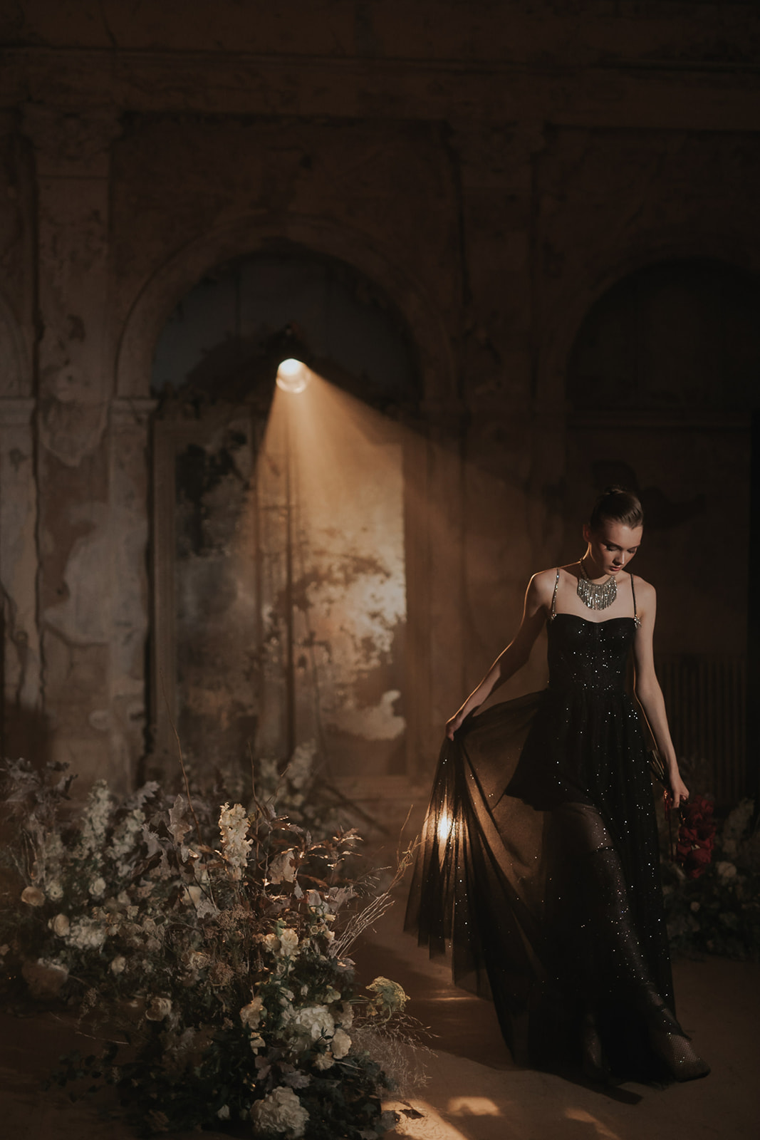 Gothic wedding inspiration with a model wearing a black glittery dress and heavy jewelry with moody flowers in a dark lit venue