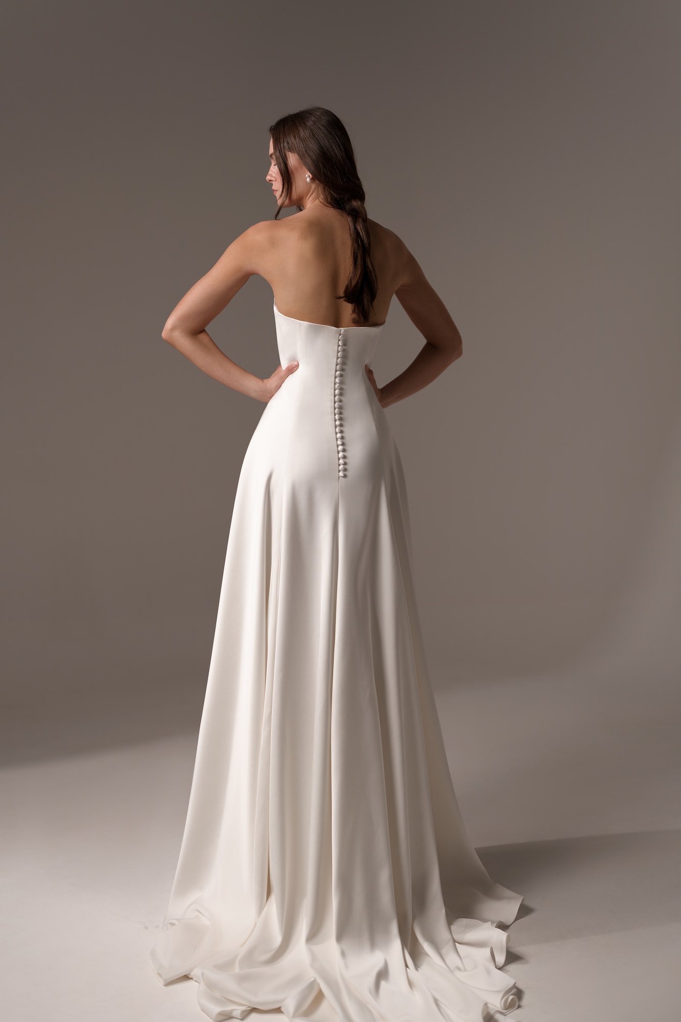 Back of Alma by Lihi Hod, minimalist silk satin A-line dreamy wedding dress with a strapless neckline and fabric-covered buttons along the back and a graceful, sweeping train.