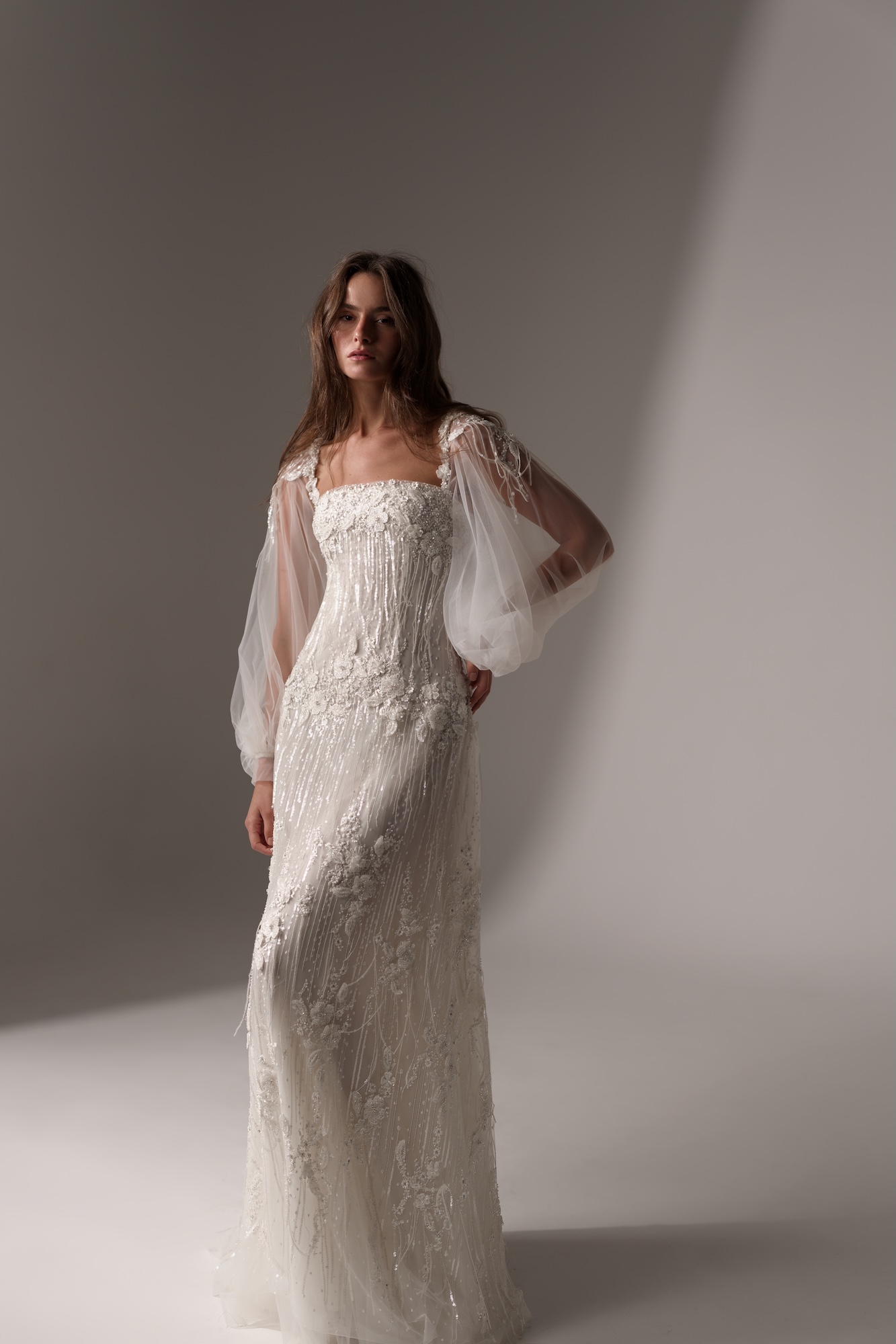 Ever, a romantic, figure-skimming gown with a refined square neckline and intricate hand-beaded floral
appliqués throughout. Sheer, voluminous tulle sleeves with beaded fringe embellishments add an ethereal touch