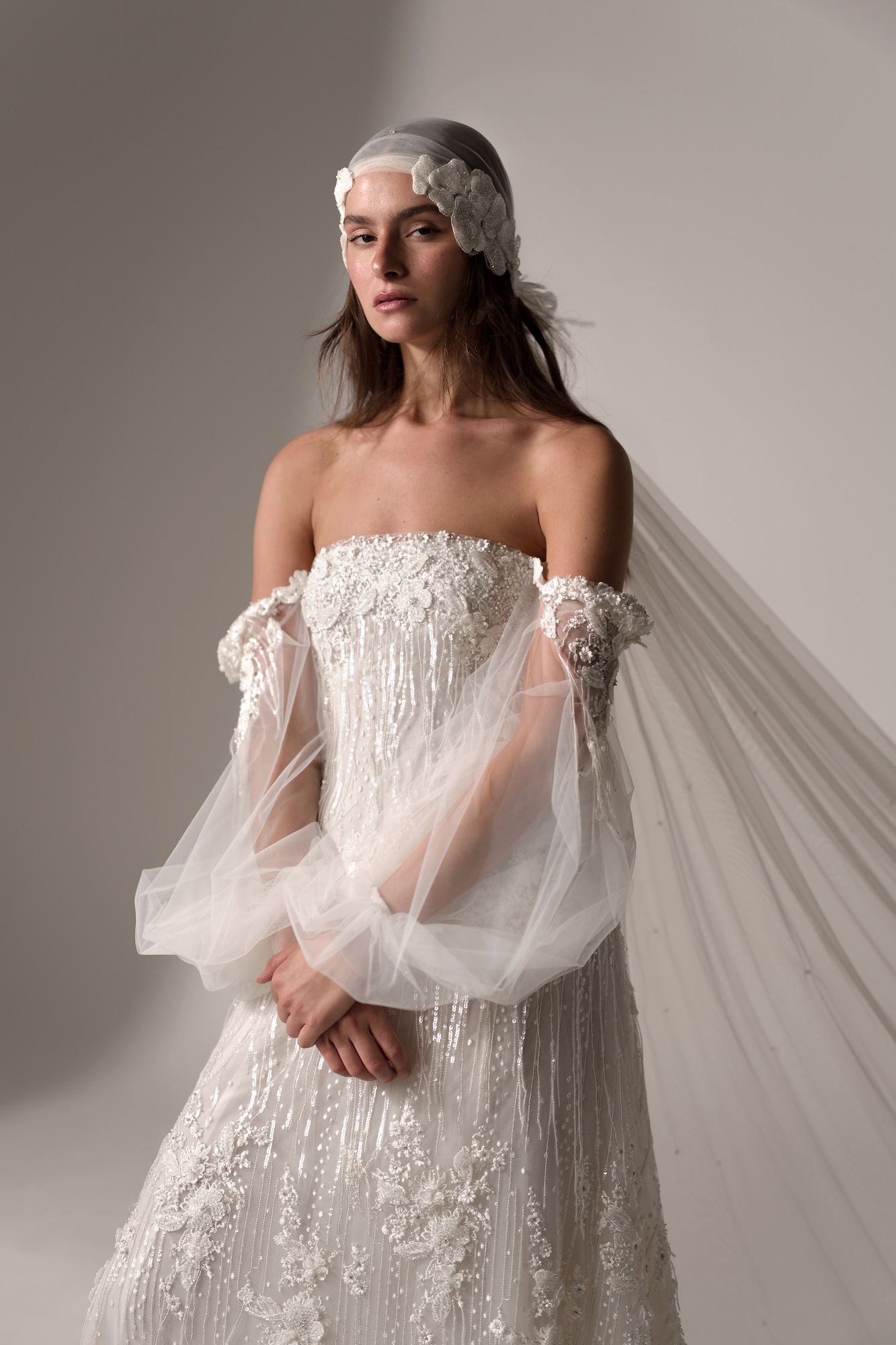 Ever by Lihi Hod, figure-skimming wedding dress with hand-beaded floral appliqués and sheer off-shoulder tulle sleeves, and tulle head scarf veil with beaded floral appliqués