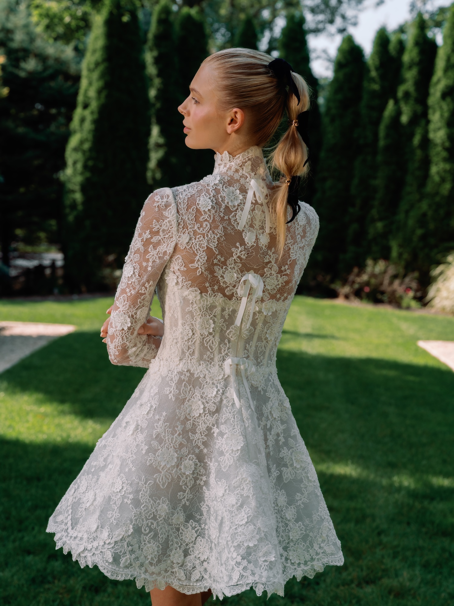 Backside portrait of the bride in Alencon Lace mini dress, with high neck fitted long sleeve and bows down the back