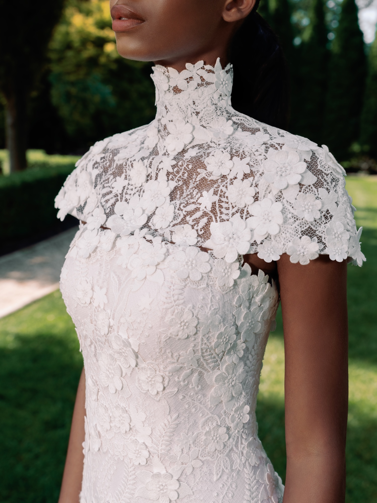 Closeup of the bride in timeless fitted wedding dress with three dimensional embroidered floral motif lace, and a matching capelet on her shoulders.