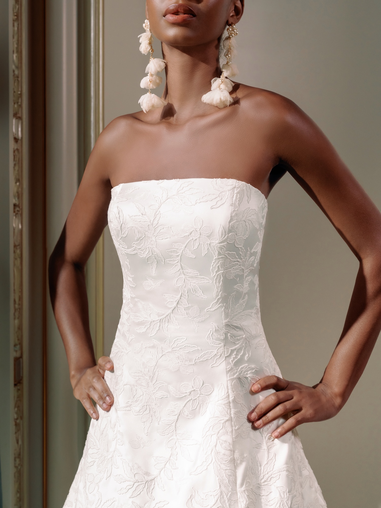 Closeup bridal portrait of the bride with long earrings and embroidered satin wedding dress, with straight across neckline