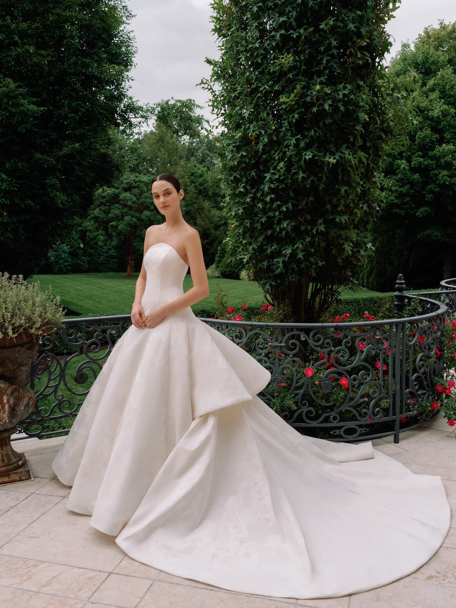 Bride standing in a luxury porch in her floral printed radzimir wedding dress with crescent moon neckline, princess seams, tiered dramatic train and ball gown skirt.