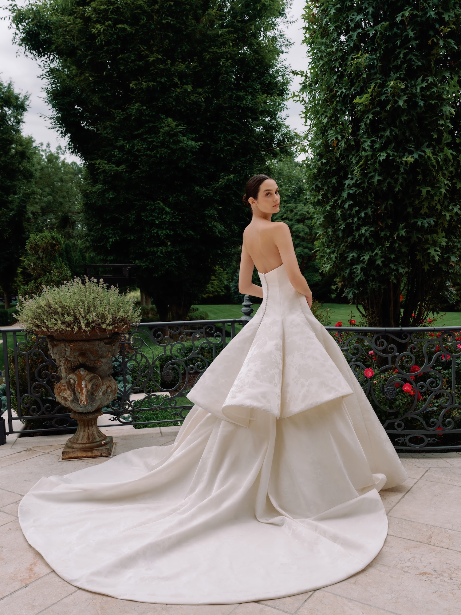 Bride standing in a luxury porch showing us the back of her floral printed radzimir wedding dress with  princess seams and tiered dramatic train and ball gown skirt.