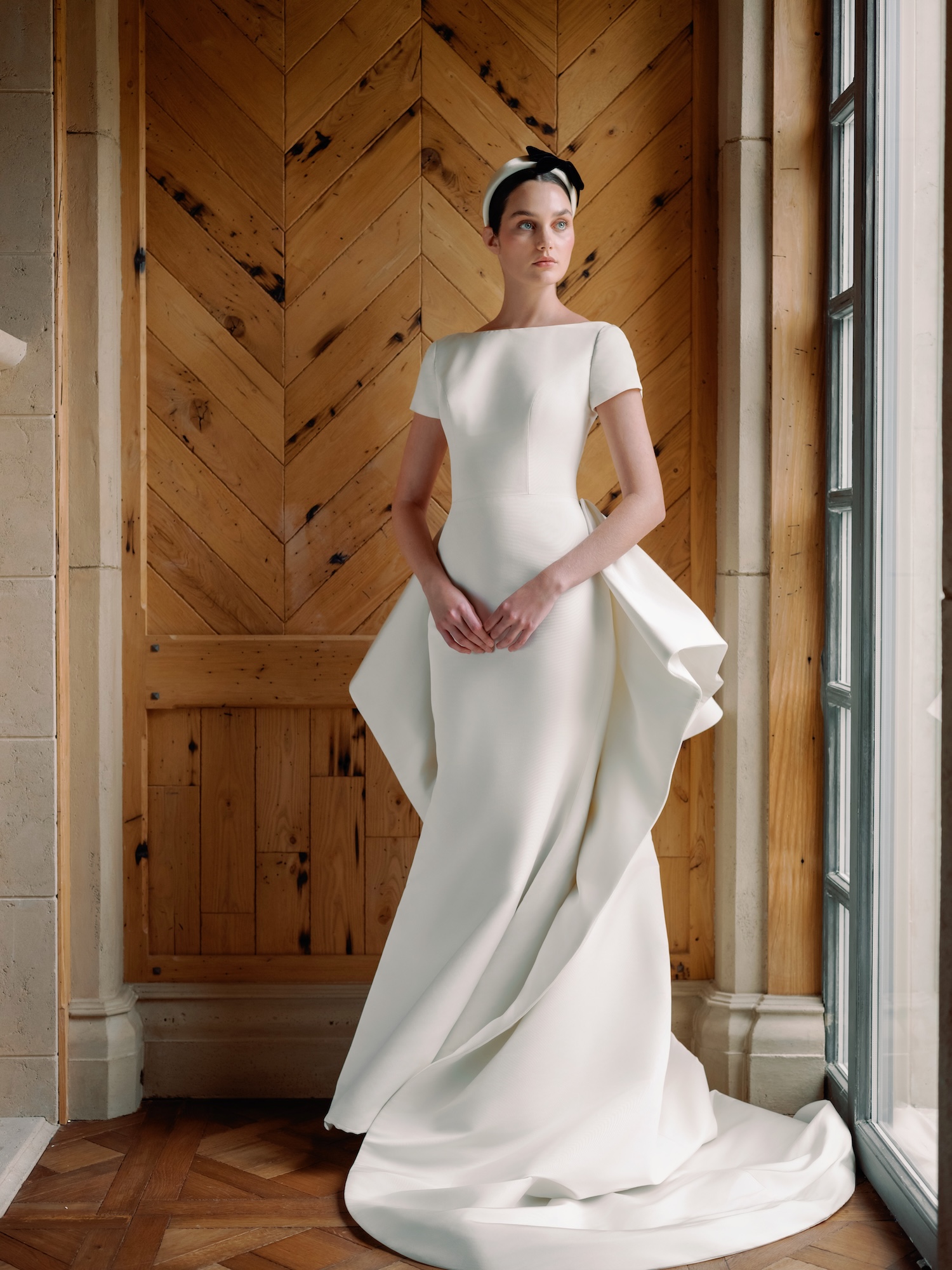White Glove wedding dress with silk faille, boat neck cap sleeve, low scoop back neckline with slim flare gown and dramatic ruffle overskirt and black headpiece