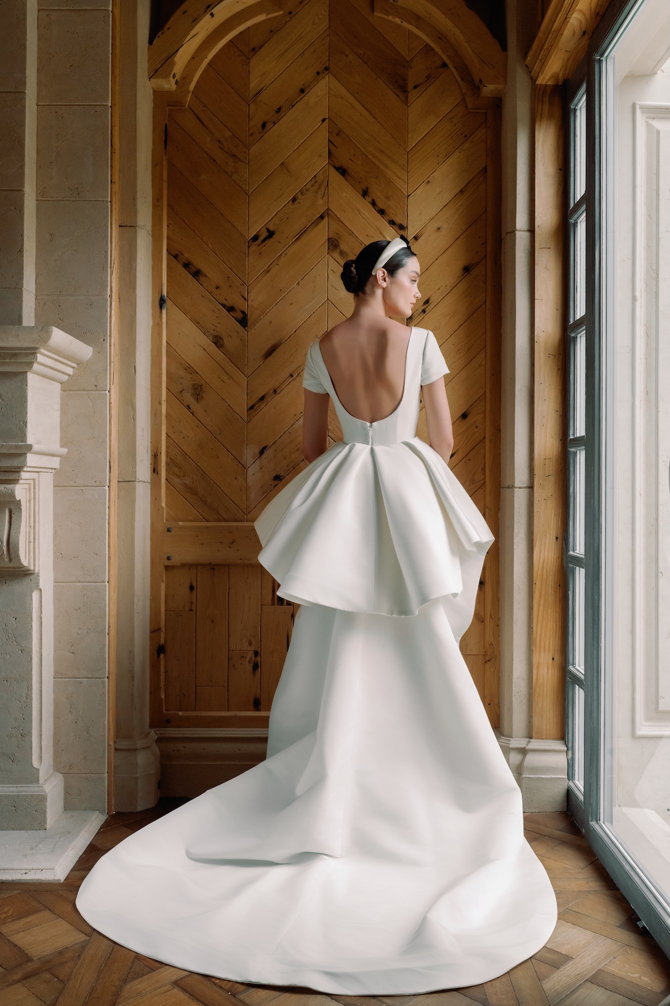 Model posing with open back silk faille wedding dress and dramatic ruffle overskirt