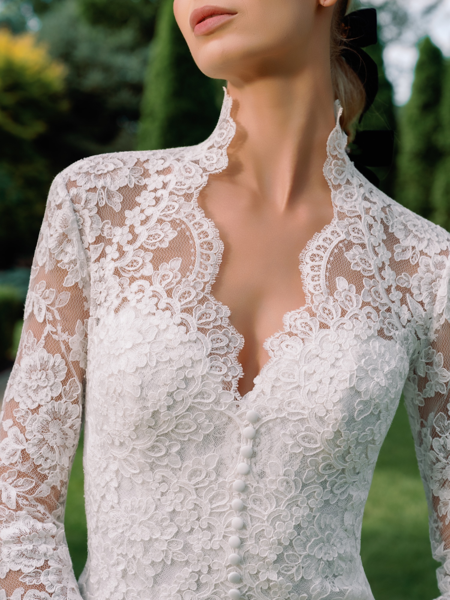 Close-up portrait of bridal dress with Alencon lace queen ann collar, fitted long sleeves, with scallop trim at neckline, with button details down the center front.